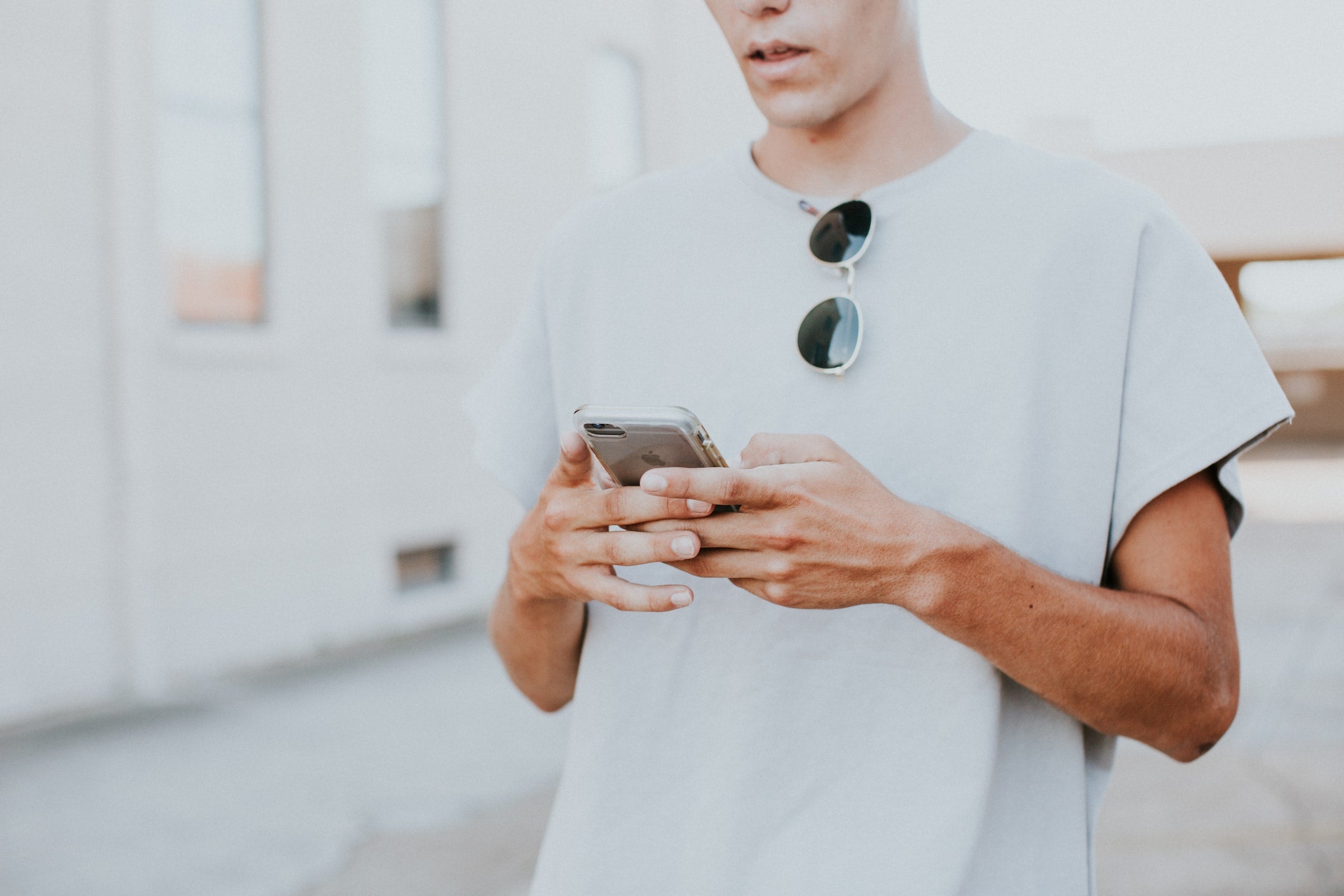 Man in white t-shirt checking social media on his phone.