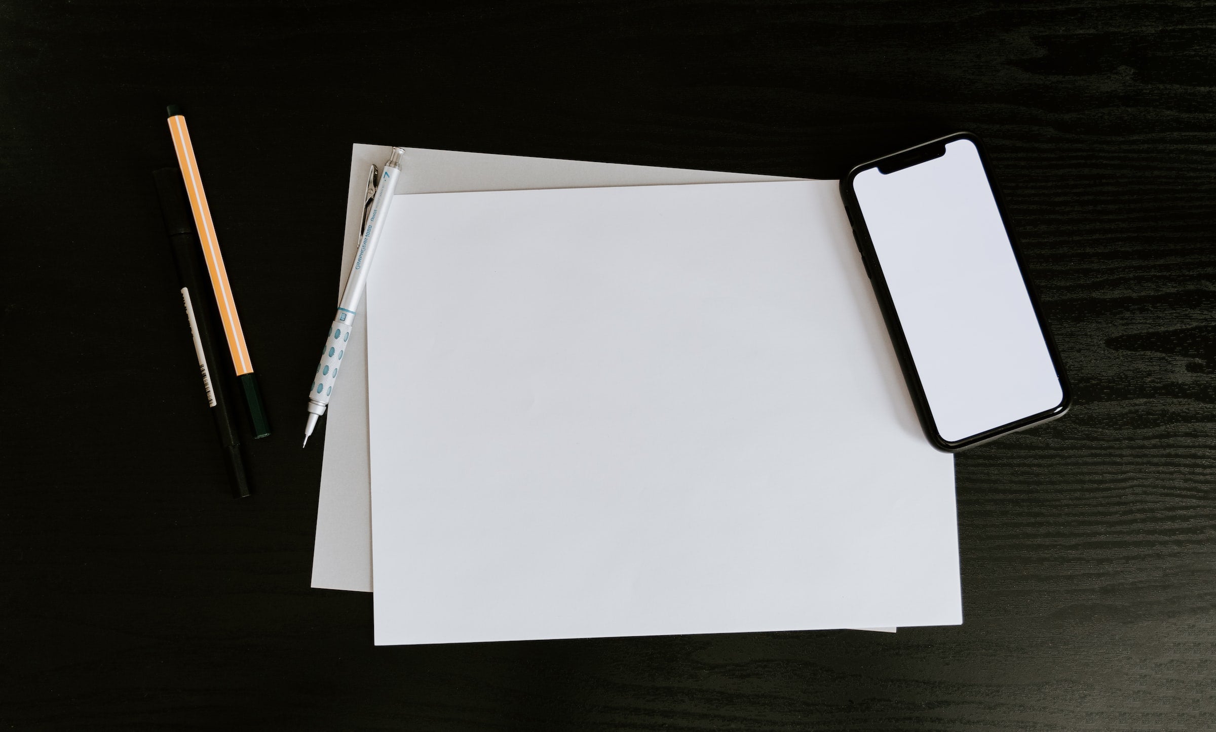 Blank drawing paper surrounded by pens and pencils.