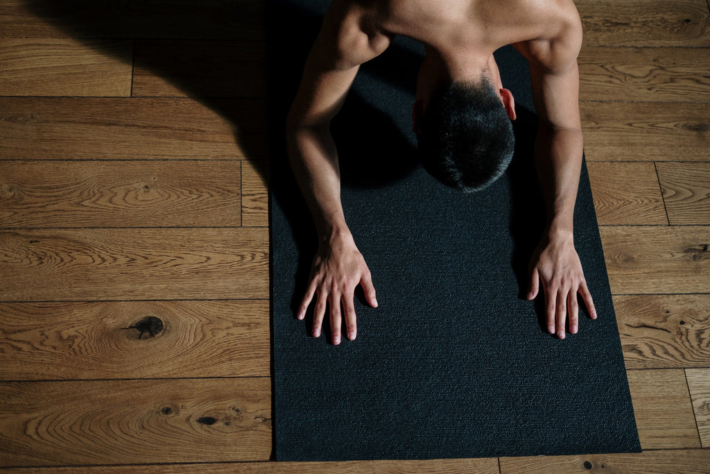 Topless man meditating on a black yoga mat.