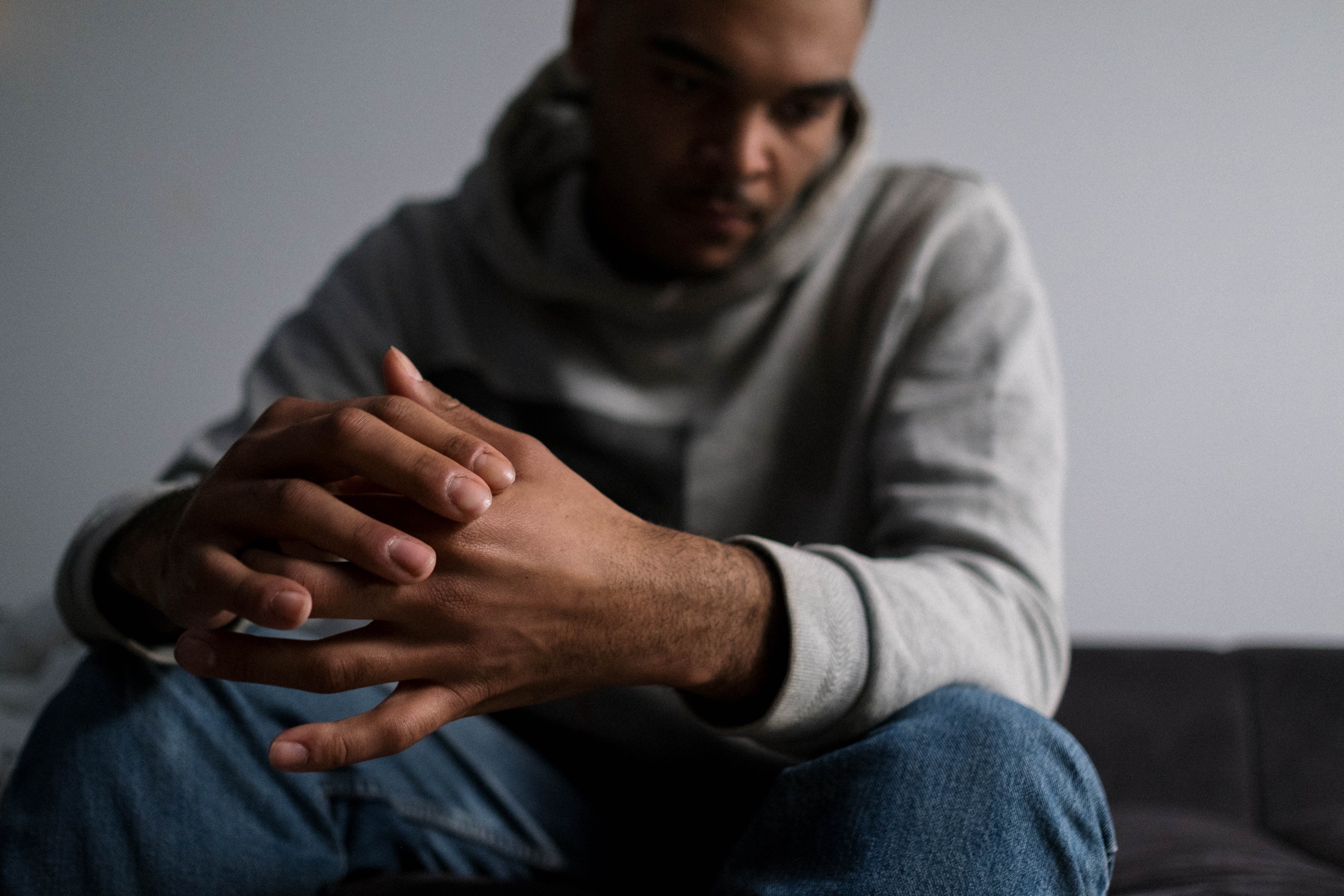 Man in grey hoodie looking down at his hands feeling stressed.